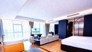 A modern hotel room with a large bed, a sofa, a TV, and a desk with a plant.