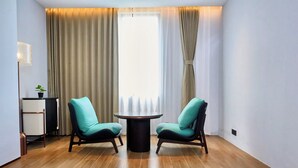 A modern room with a round table, two chairs, a potted plant, a lamp, and a view through sheer curtains.