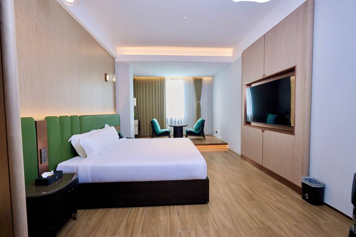 Habitación de hotel con una cama grande, televisor, una mesita pequeña, dos sillas y vistas al exterior.