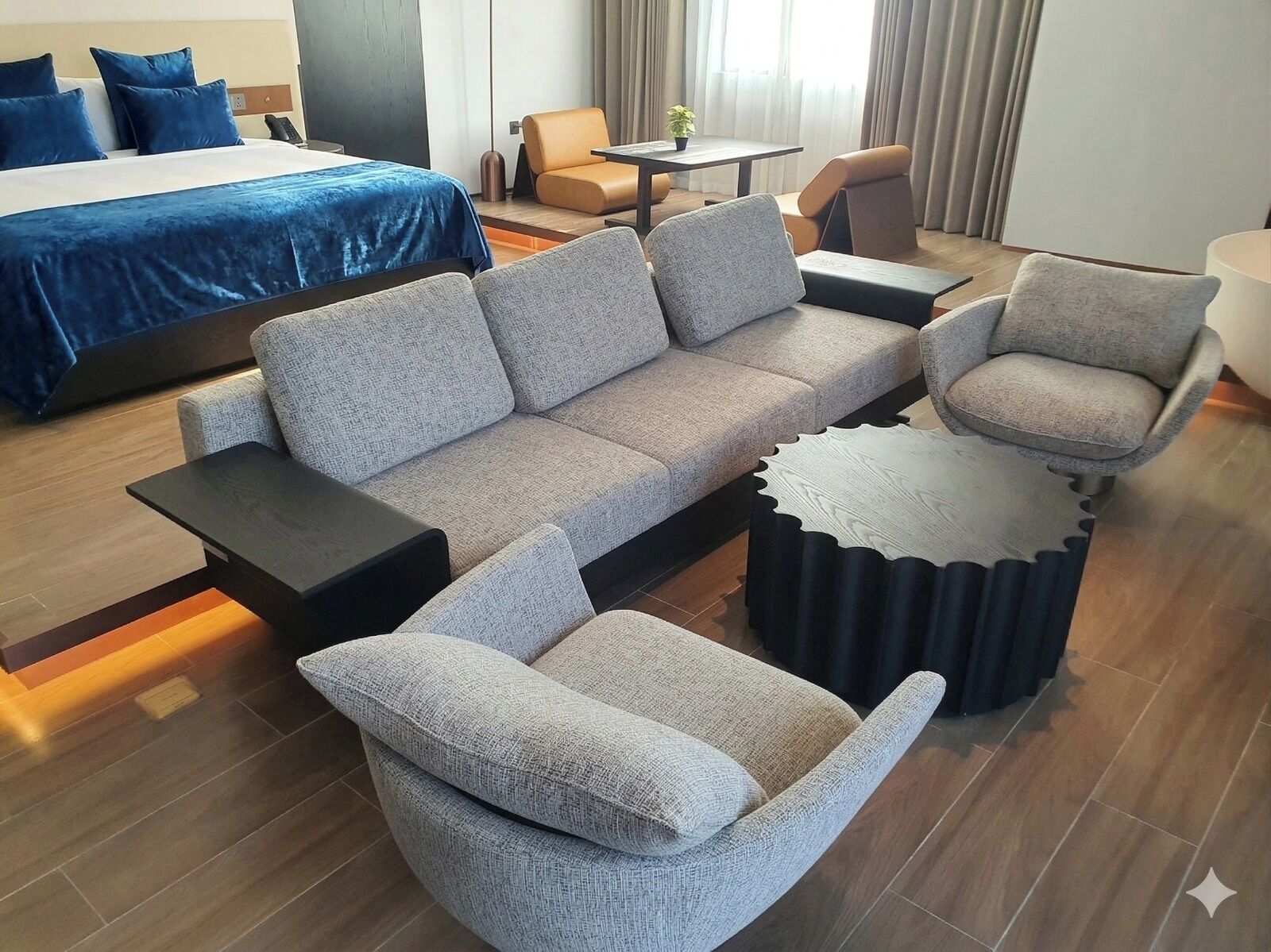 Una camera d'hotel moderna con un letto grande, un divano grigio, due poltrone, un tavolino e un originale tavolo da caffè rotondo.