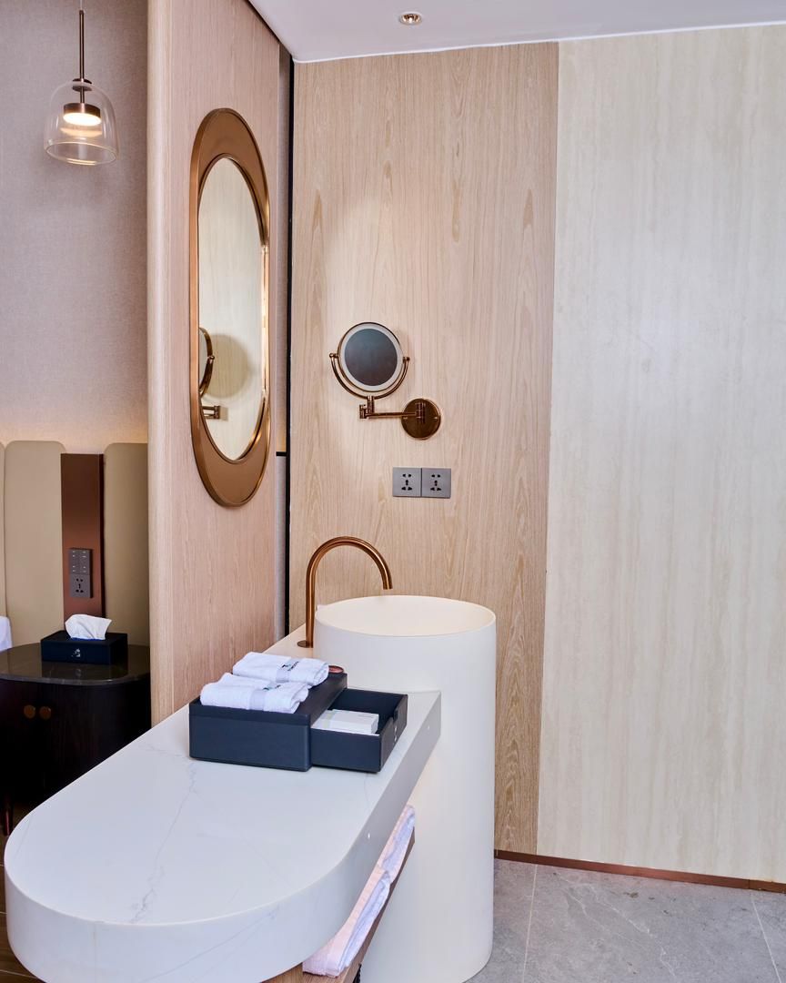 A modern bathroom with a freestanding bathtub, a round mirror, and a wall-mounted sink with a copper faucet.
