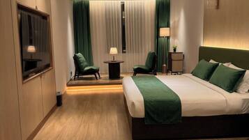A modern hotel room with a large bed, two chairs, a small table, a TV, and a window with curtains.