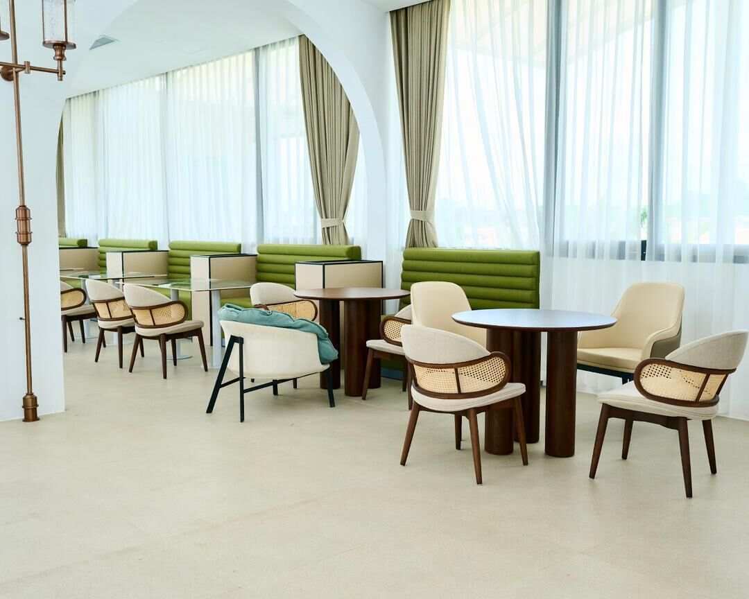 A modern hotel lobby with green seating areas, round tables, and wicker chairs.