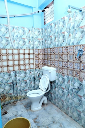 Casa de banho com sanita, chuveiro e paredes em azulejo.