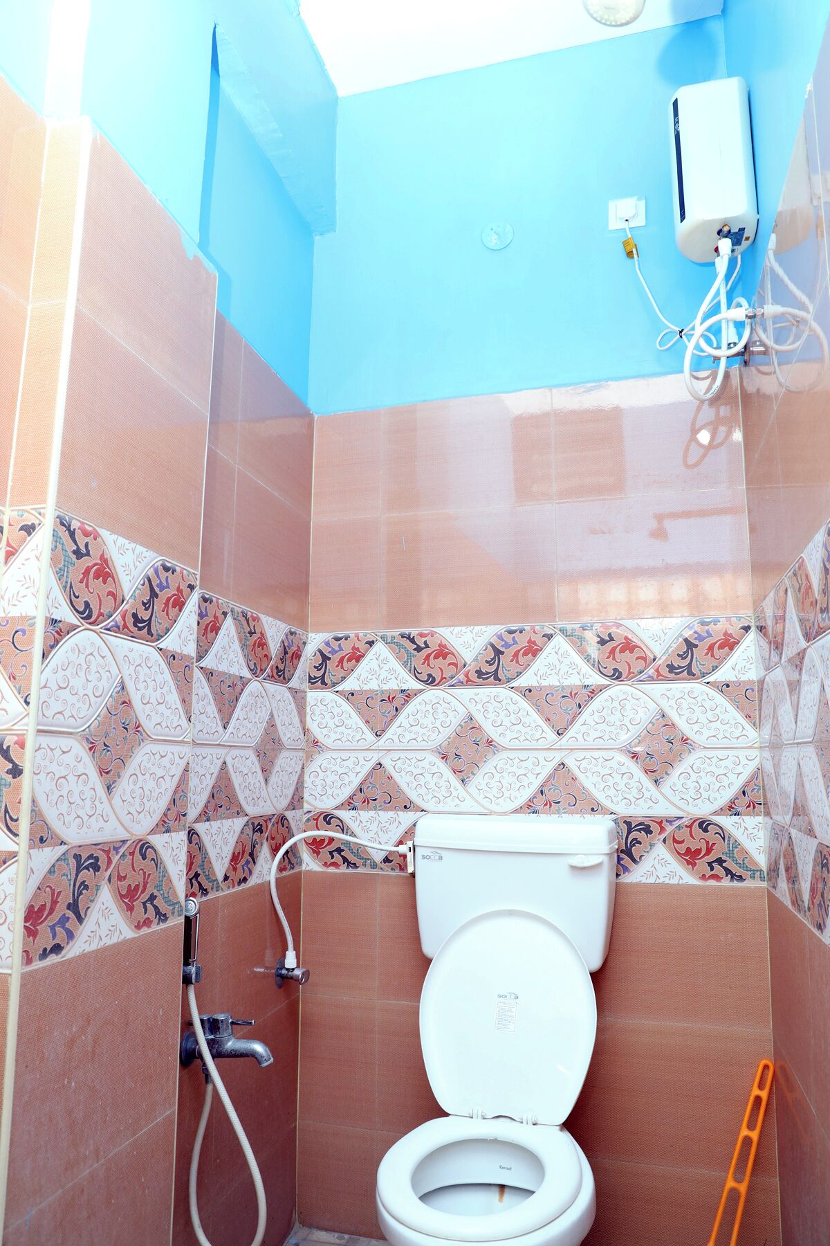 Une salle de bain avec des carreaux décorés, des toilettes, un sèche-mains et une prise électrique visible.