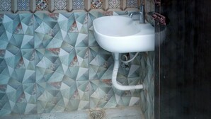 A bathroom with a geometric tile backsplash, a white sink, and a shower enclosure. - Akshaya Mahal A/C Rooms (Anapirandan)