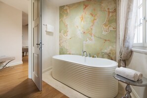 Ein modernes Badezimmer mit freistehender Badewanne, Marmorwand und einem kleinen Tisch mit einem Handtuch.
