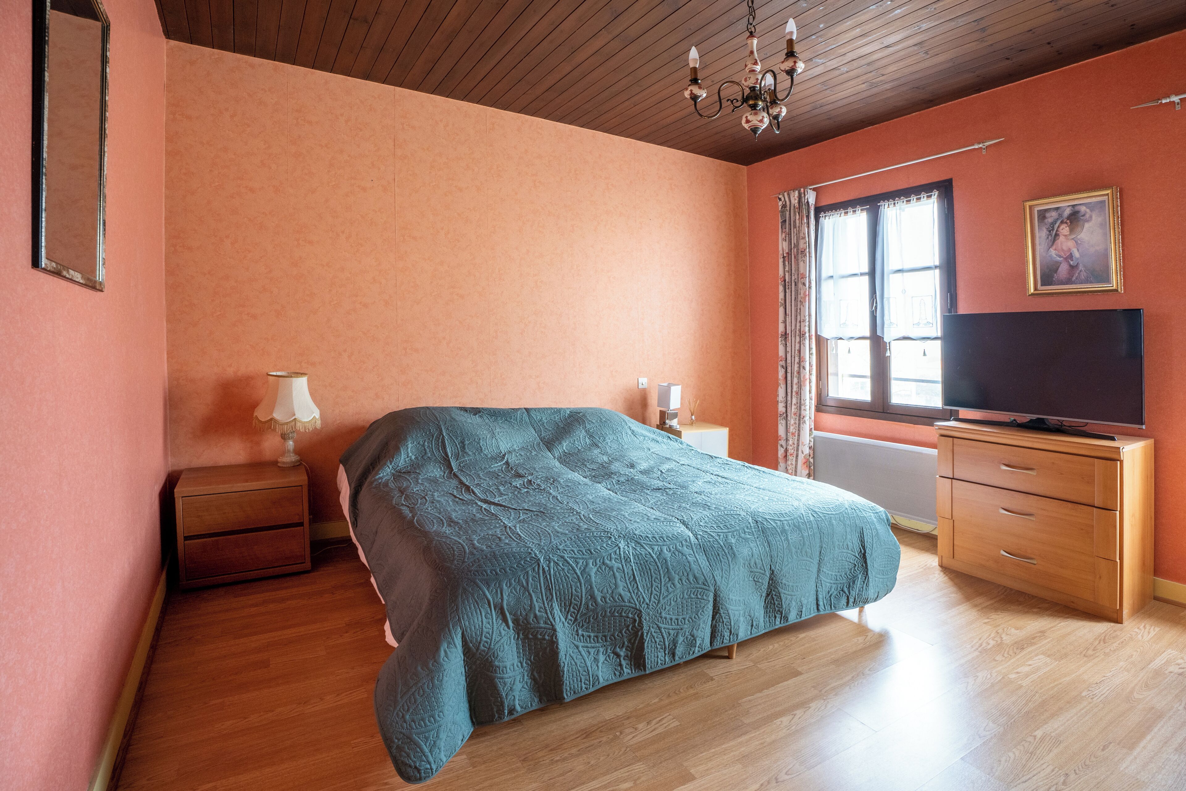 Ein Schlafzimmer mit Bett, Fernseher, Nachttisch, Kommode und einem Fenster mit Vorhängen.