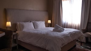 Quarto de hotel com uma cama grande, duas luminárias de cabeceira, uma cadeira e uma janela com cortinas.