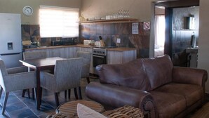Um espaço compacto com área de refeições, sofá, cozinha equipada com fogão e micro-ondas, e um banheiro visível por uma porta aberta.