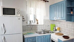 Een kleine keuken met een magnetron, fornuis, spoelbak en blauwe kastjes.