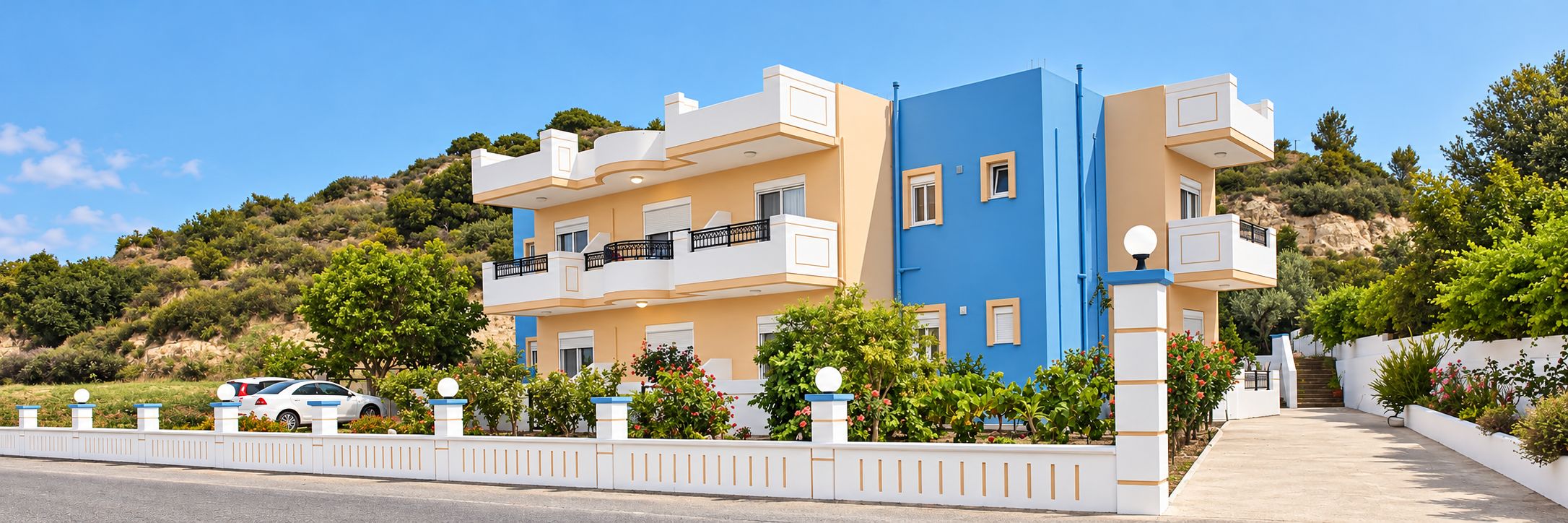 A multi-story residential building with balconies, a white fence, and a driveway.
