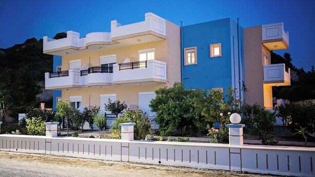 Een meerlaags woongebouw met balkons, een gevel in wit en blauw, en een aangelegde tuin.