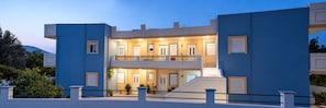 A modern two-story building with a balcony, multiple doors, and potted plants. - Garden-View Apartment with Private Courtyard (Faliraki)
