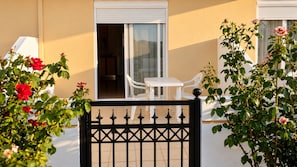 A gated balcony with a white table and chairs, a sliding glass door, and rose bushes. - Garden-View Apartment with Private Courtyard (Faliraki)