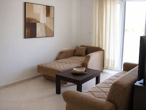 A living room with a sofa, a coffee table, and a painting on the wall. - Garden-View Apartment with Private Courtyard (Faliraki)