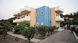 Een gebouw met twee verdiepingen, balkons, een blauw middenstuk en veel groen eromheen.