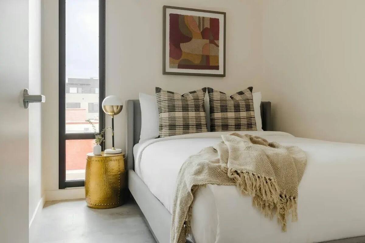 Una camera da letto con un letto, una finestra, un quadro incorniciato e un comodino con una lampada.