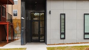 A modern building entrance with a glass door, a staircase, and a small outdoor area with grass. - The Artesian (Denver)