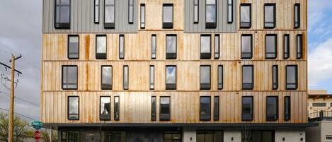A multi-story building with a modern design, featuring a combination of wooden and metal panels, large windows, and a flat roof.