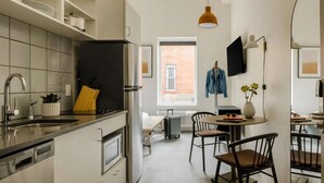 A compact kitchen with a modern refrigerator, a sink, and a dining area with chairs and a table. - The Artesian (Denver)