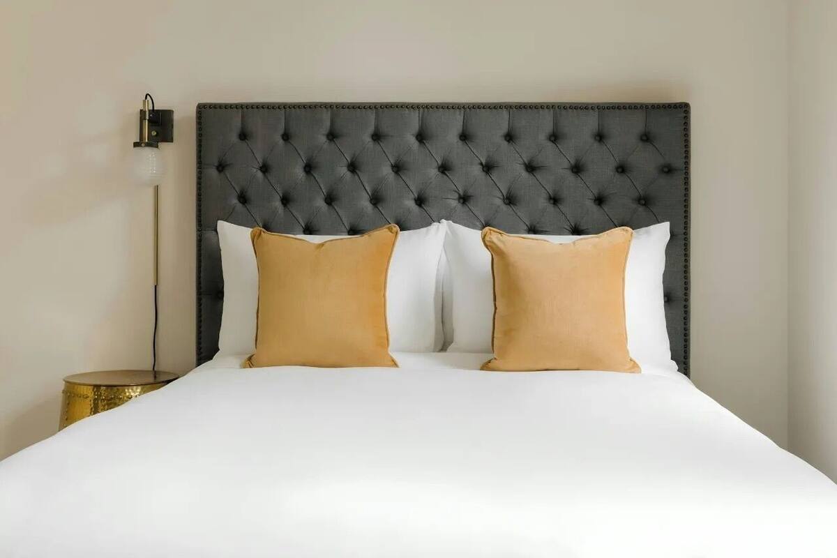 Un letto con testiera imbottita, due cuscini e una lampada da comodino.