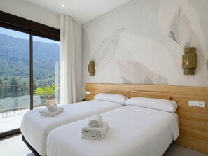 Ein Hotelzimmer mit zwei Betten, einem großen Fenster mit Bergblick und einer Wand mit Blättermotiv.