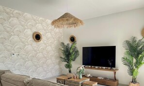 Ein Wohnzimmer mit Wandmuster, einem Fernseher, einer Couch und zwei Blumentöpfen.