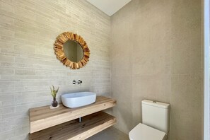 Een badkamer met een houten wastafelmeubel, een ronde spiegel en een toilet.