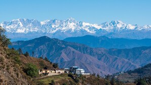 A mountainous landscape with snow-capped peaks, a cluster of buildings on a hillside, and terraced fields below. - The Celebrè- A Little Castle Homestay  (Tehri)