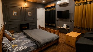 A bedroom with a bed, a TV, a fireplace, and a wooden bench. - The Celebrè- A Little Castle Homestay  (Tehri)