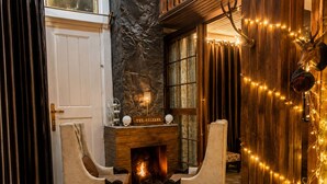A cozy room with a fireplace, two armchairs, a stone wall, and a wooden door. - The Celebrè- A Little Castle Homestay  (Tehri)