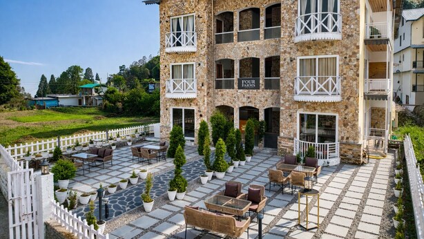 A multi-story building with a stone facade, outdoor seating area, and a sign reading 'FOUR FARMS.' - Four Farm - Best Resort In Nainital For Family (Nainital)