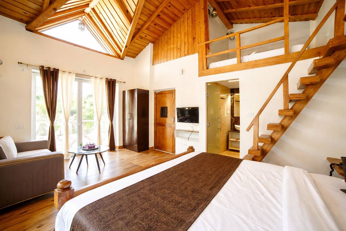 A bedroom with a large bed, a sofa, a wooden staircase, and a TV.