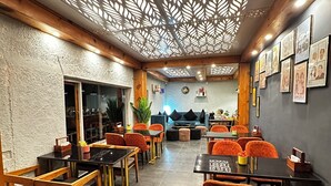 A restaurant interior with wooden tables and chairs, a patterned ceiling, and framed pictures on the walls. - Four Farm - Best Resort In Nainital For Family (Nainital)