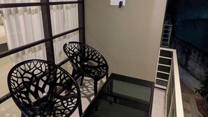 Ein Balkon mit einem Glastisch und zwei Stühlen, eine Steckdose an der Wand und Blick ins Freie.