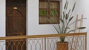 Un balcón con una maceta, una puerta de madera y una ventana con celosías metálicas decorativas.