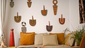 Una sala de estar con un sofá, cojines, un jarrón rojo, una mesa de madera y adornos en la pared.