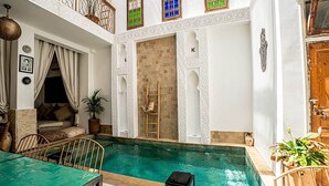 Una piscina interior con solárium de madera, zona de comedor y área de descanso con vistas a la piscina.