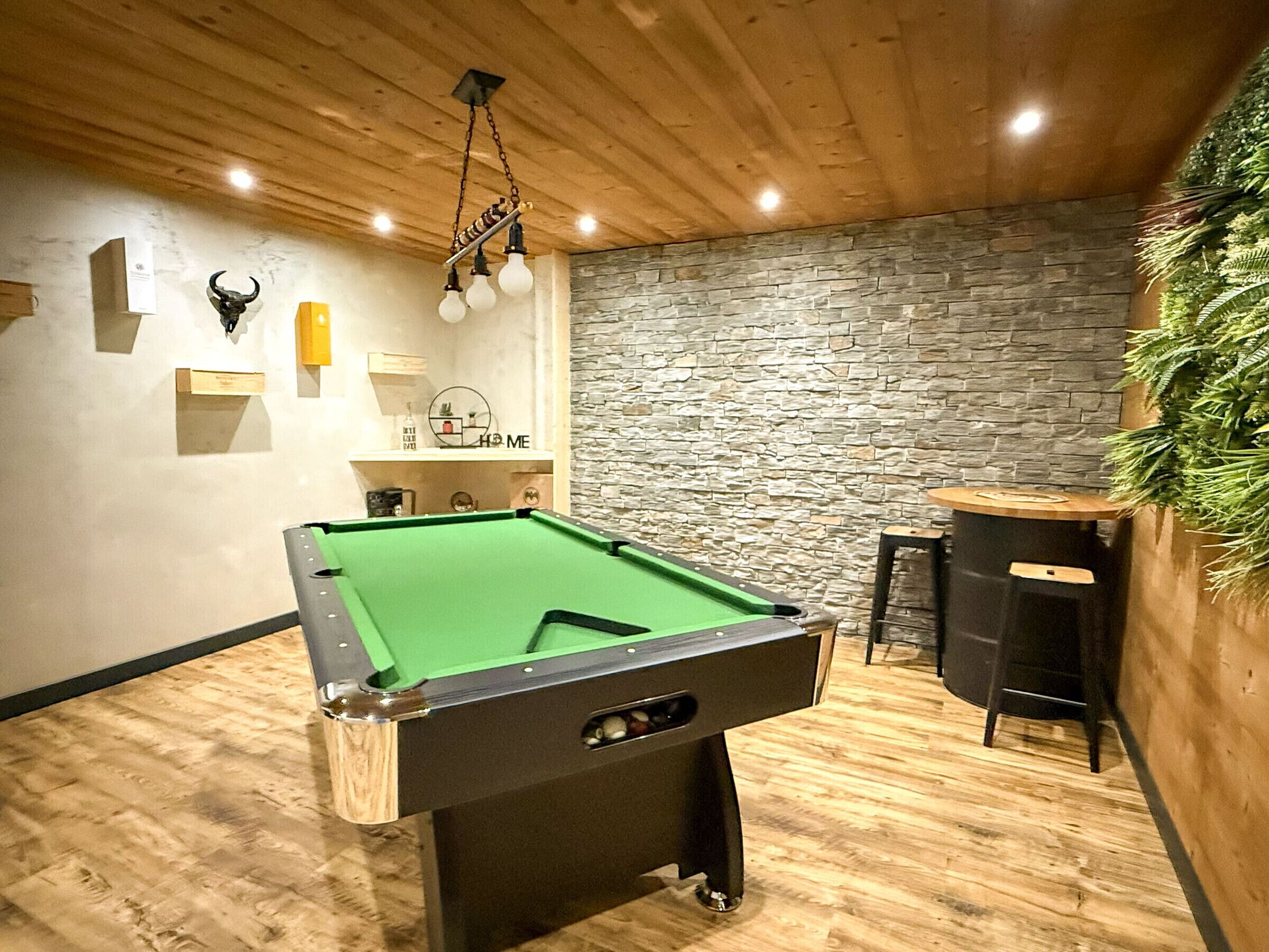 A pool table in a room with wooden flooring, a stone wall, and a hanging light fixture.