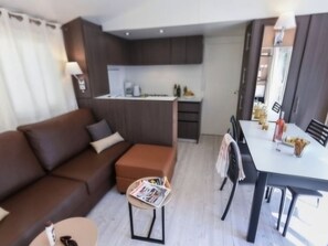 Ein modernes Wohnzimmer mit einem braunen Sofa, einem kleinen runden Tisch mit Zeitschriften und einem Essbereich mit einem weißen Tisch und Stühlen.