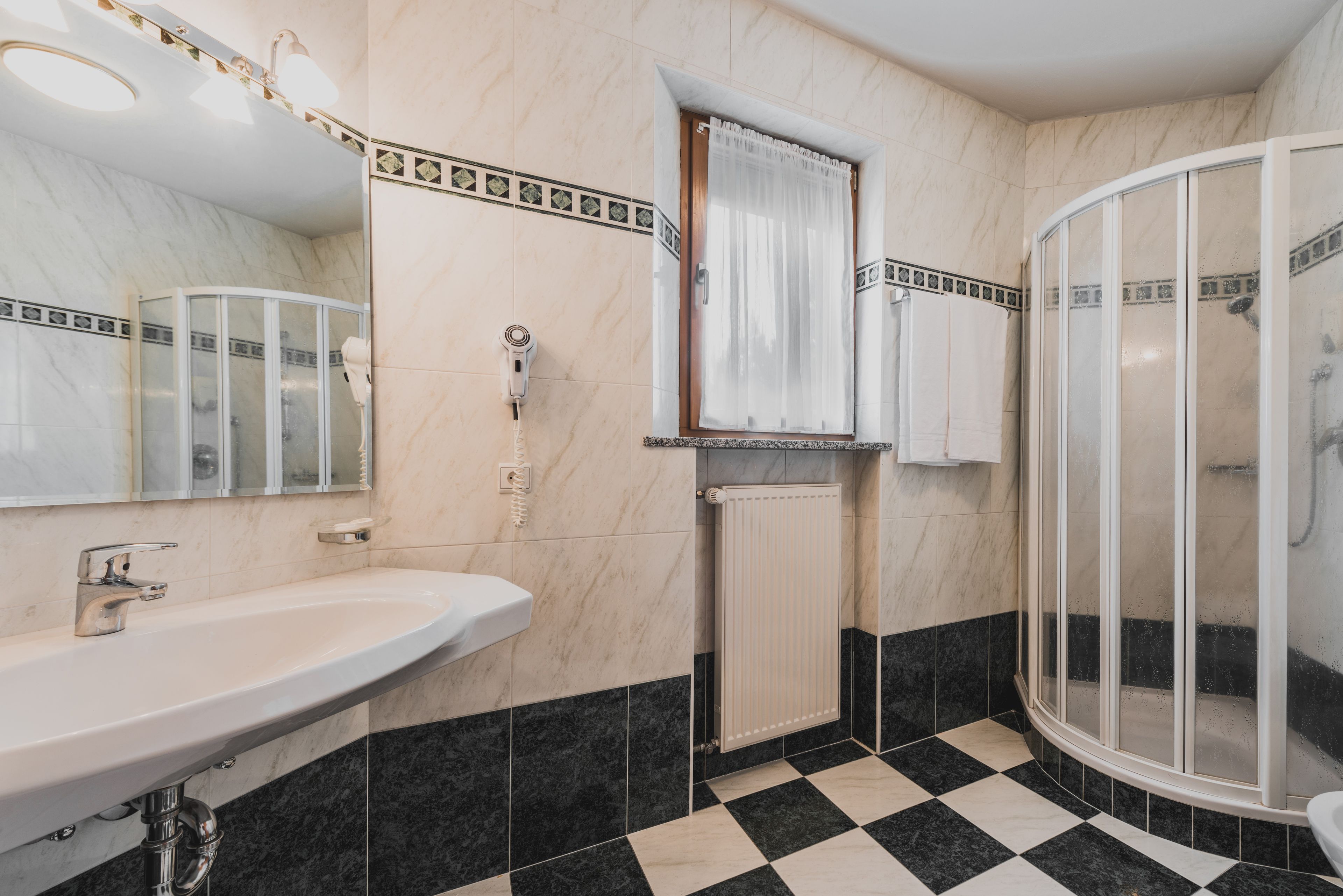 Un bagno con un lavandino bianco, uno specchio, una doccia con porta in vetro e un pavimento piastrellato.