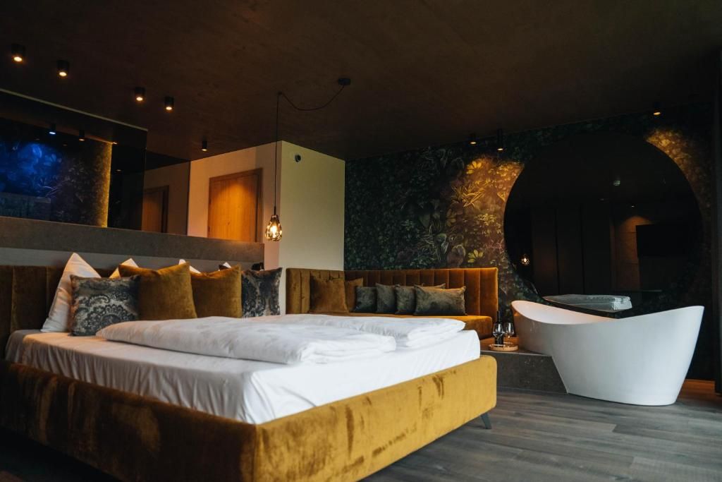 Une chambre moderne avec un grand lit, un canapé, une baignoire et un mur en pierre.