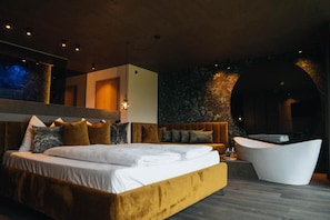 Une chambre moderne avec un grand lit, un canapé, une baignoire et un mur en pierre.