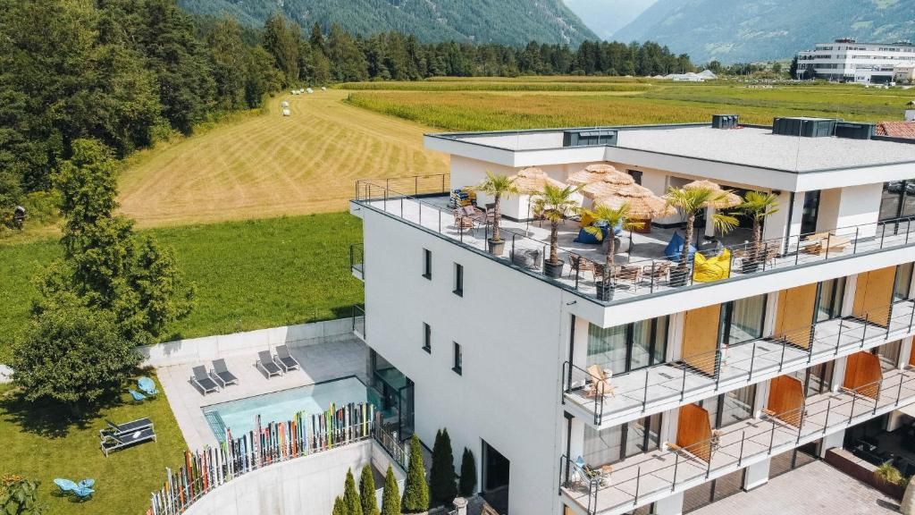 Un bâtiment moderne doté d’une terrasse sur le toit, d’une piscine et offrant une vue sur un champ verdoyant et des montagnes.