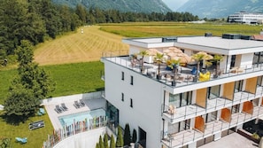 Un bâtiment moderne doté d’une terrasse sur le toit, d’une piscine et offrant une vue sur un champ verdoyant et des montagnes.