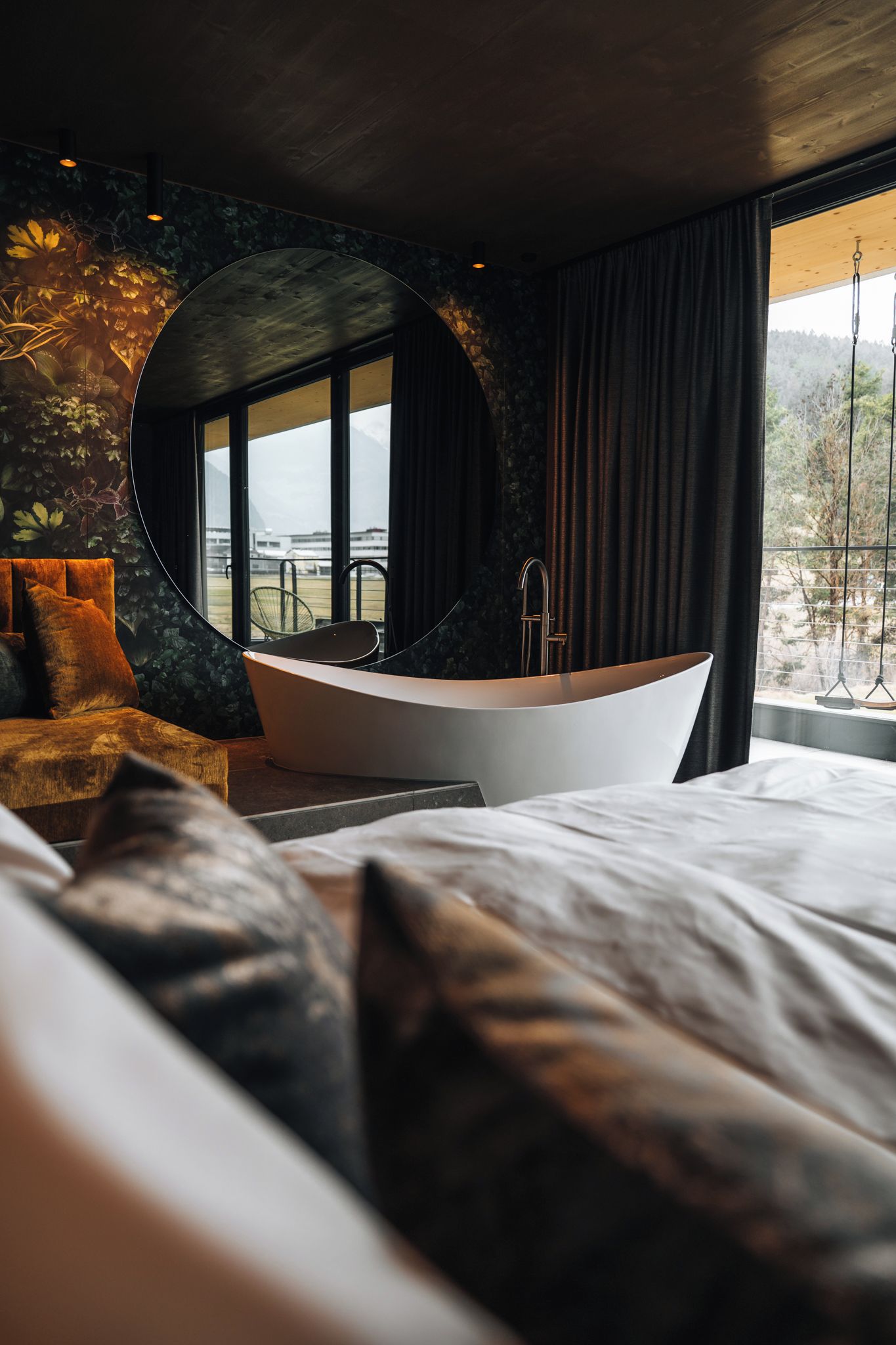 Ein modernes Schlafzimmer mit einem großen Bett, einem runden Spiegel, einer Badewanne und Blick ins Freie.