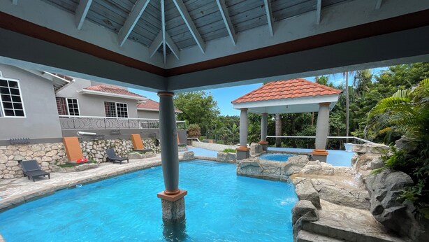 A swimming pool with stone steps and a gazebo, surrounded by a stone wall and lounge chairs. - 3-bedroom luxurious house in Kingston with pool, private parking free WiFi (Kingston)