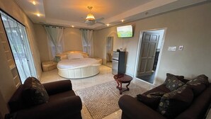A bedroom with a bed, a ceiling fan, a TV, a sofa, and a dining area with a refrigerator. - 3-bedroom luxurious house in Kingston with pool, private parking free WiFi (Kingston)