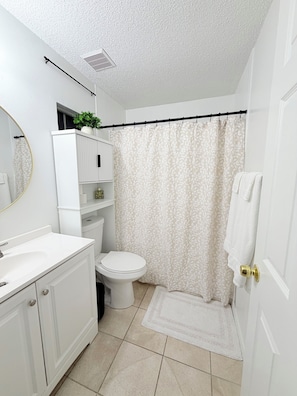 Un baño con inodoro, lavabo, espejo, cortina de ducha y toallero.